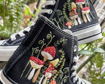 May include: Black high-top canvas shoes with embroidered mushrooms and greenery. The shoes have white laces and a white rubber sole.