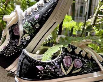 May include: A pair of black canvas sneakers with white soles and laces. The sneakers are decorated with embroidered purple and green flowers.