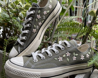 May include: A pair of green canvas low-top sneakers with white soles and white laces. The sneakers are embroidered with small pink and green flowers.