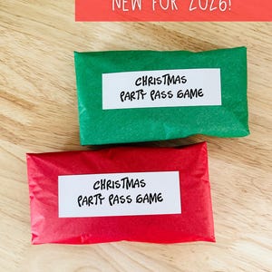 May include: Two wrapped gifts, one green and one red, with white labels that read "CHRISTMAS PARTY PASS GAME." A red banner at the top says "NEW FOR 2026!" on a wooden surface.