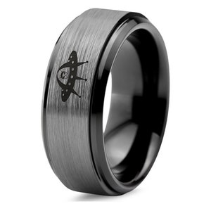 May include: A black tungsten carbide ring with a brushed finish and a black polished edge. The ring features a laser-engraved UFO design.