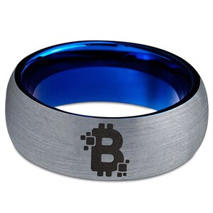 Op de afbeelding: Een zilveren ring van wolfraamcarbide met een blauwe binnenband en een zwart Bitcoin-symbool gegraveerd aan de buitenkant.