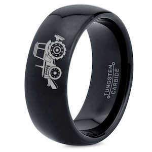 May include: A black tungsten carbide ring with a silver tractor design engraved on the side. The ring is inscribed with "TUNGSTEN CARBIDE" on the inside.