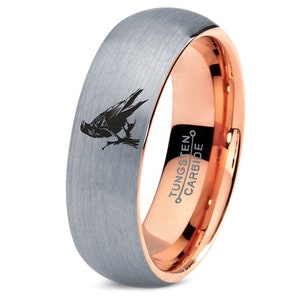 May include: A silver tungsten carbide ring with a rose gold band. The ring features a black raven design and the words "TUNGSTEN CARBIDE" engraved on the rose gold band.
