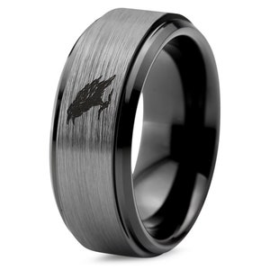 May include: A black tungsten carbide ring with a brushed finish and a black beveled edge. The ring features a black raven design on the top.