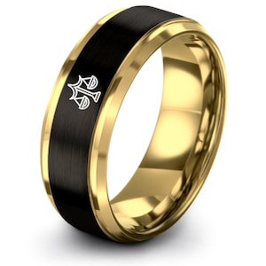 Op de afbeelding: Een goudkleurige ring met een zwarte middenband. De ring heeft een wit embleem op de zwarte band. De ring heeft een gepolijste afwerking en een klassiek ontwerp.