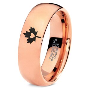 May include: Rose gold tungsten carbide ring with a black engraved Canadian maple leaf with a heart in the center. The ring is inscribed with "TUNGSTEN CARBIDE".