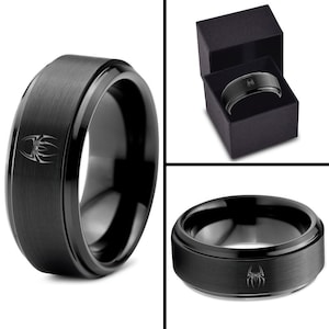 May include: A black tungsten carbide ring with a brushed finish and a spider design. The ring is in a black box.