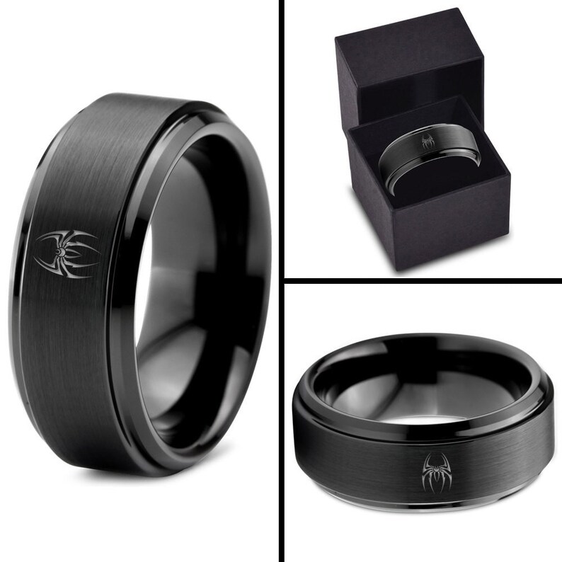 May include: A black tungsten carbide ring with a brushed finish and a spider design. The ring is in a black box.