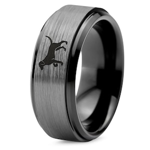 May include: A black tungsten carbide ring with a brushed finish and a black inlay. The ring features a silhouette of a dog on the brushed surface.