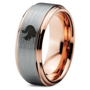 May include: A silver tungsten carbide ring with a rose gold band and a black squirrel silhouette engraved on the top.