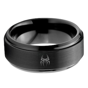 May include: A black tungsten carbide ring with a brushed finish and a black spider design engraved on the band.
