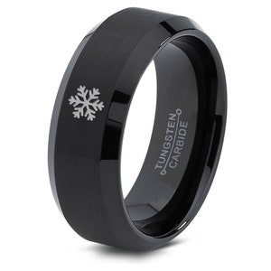 May include: Black tungsten carbide ring with a beveled edge and a snowflake design. The ring is engraved with "TUNGSTEN CARBIDE".