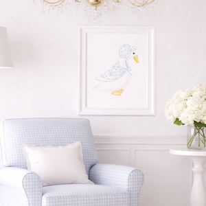May include: A framed watercolor print of a goose wearing a bonnet hangs above a blue and white checkered armchair with a white pillow. A white side table holds a vase of white flowers. A gold floor lamp and chandelier complete the nursery decor.