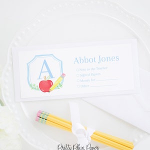 May include: A white card with a blue border and a watercolour illustration of a red apple, a pencil, and the letter A. The card has the text "Abbot Jones" and a checklist with the options "Note to the Teacher", "Signed Papers", "Money for", and "Other".