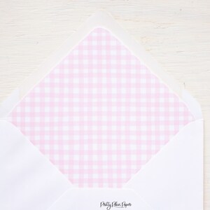 Pode incluir: Um envelope branco com um forro de xadrez rosa na aba interna. O envelope está dobrado e a aba está fechada. O texto "Pretty Plain Paper" está impresso na parte inferior do envelope.