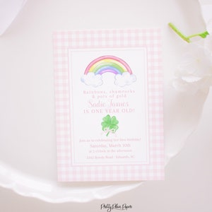May include: A pink and white gingham patterned invitation with a rainbow, shamrocks, and the text "Rainbows, shamrocks & pots of gold Sadie James is one year old!"  Join us in celebrating her first birthday! Saturday, March 10th at 2 o'clock in the afternoon. 3342 Itowdy Road-Edwards, SC. Pretty Plain Paper.
