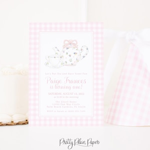Puede incluir: Una invitación rosa y blanca a cuadros para una fiesta de primer cumpleaños. La invitación presenta una ilustración de tetera y taza de flores. El texto dice "¡Paige Frances cumple un año!" e incluye detalles del evento. También se ve un gorro de fiesta a juego.