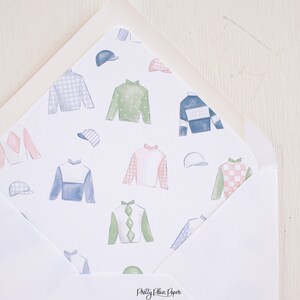 May include: A white envelope featuring a colourful pattern of jockey silks and hats. The envelope is folded in half, with the pattern visible on the front and back. The text "Pretty Plain Paper" is printed on the bottom of the envelope.