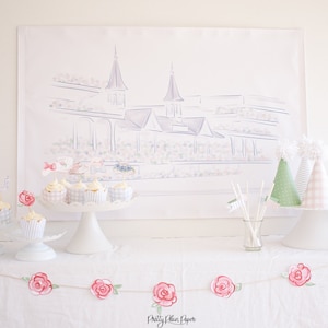 May include: A table setting for a party with a white tablecloth, a white cake stand with cupcakes, and a banner with the text "Pretty Plain Paper". There are also party hats and a drawing of a racetrack in the background.
