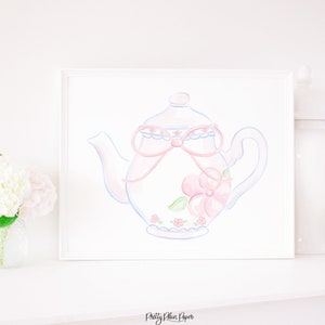 Puede incluir: Una ilustración de acuarela de una tetera rosa con un patrón floral azul y blanco y un lazo rosa. La tetera está sobre un fondo blanco.