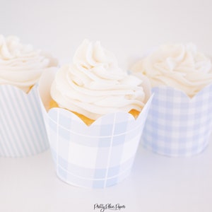 May include: Three white cupcakes with white frosting in blue and white striped and plaid cupcake liners.