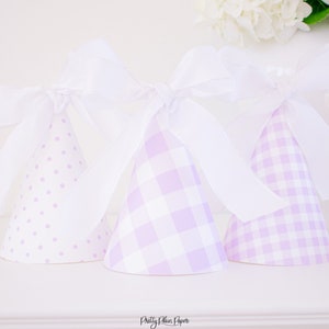 May include: Three purple and white party hats with white ribbon bows. The hats have different patterns: polka dots, gingham, and plaid.