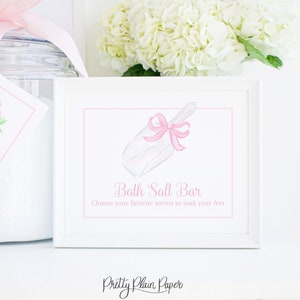 May include: A white framed sign with a pink watercolor illustration of a bath salt scoop with a pink bow. The text on the sign reads "Bath Salt Bar" and "Choose your favorite scents to soak your feet". The sign also includes the text "Pretty Plain Paper".