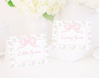 May include: Two white place cards with pink bows and a floral pattern. The text on the cards reads "Edith James" and "Lovey June".