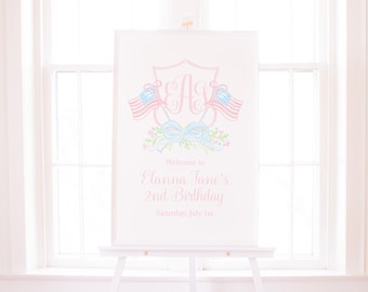 May include: A white sign with a pink and blue monogram and two American flags. The sign says "Welcome to Elanna Jane's 2nd Birthday Saturday, July 1st".