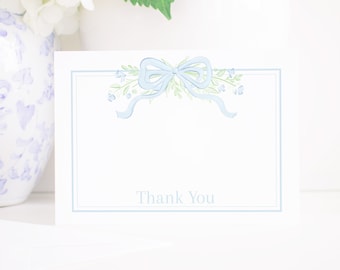 May include: A light blue thank you card featuring a watercolour illustration of a bow and floral accents. The text "Thank You" is printed in the centre of the card.