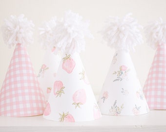 May include: Set of five pink and white party hats with white pom poms on top. Two hats feature a pink and white gingham pattern, one hat features a floral pattern, and two hats feature a strawberry pattern.
