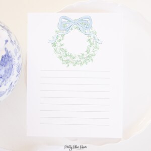 May include: A white card with a green and white wreath with a blue bow on top. The card has lined paper for writing and the text "Pretty Plain Paper" at the bottom.