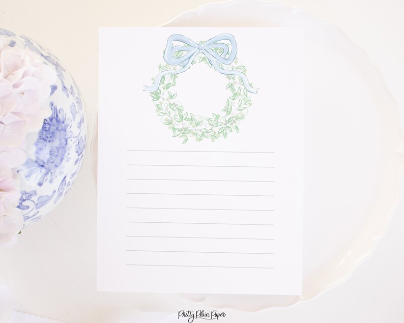 May include: A white card with a green and white wreath with a blue bow on top. The card has lined paper for writing and the text "Pretty Plain Paper" at the bottom.