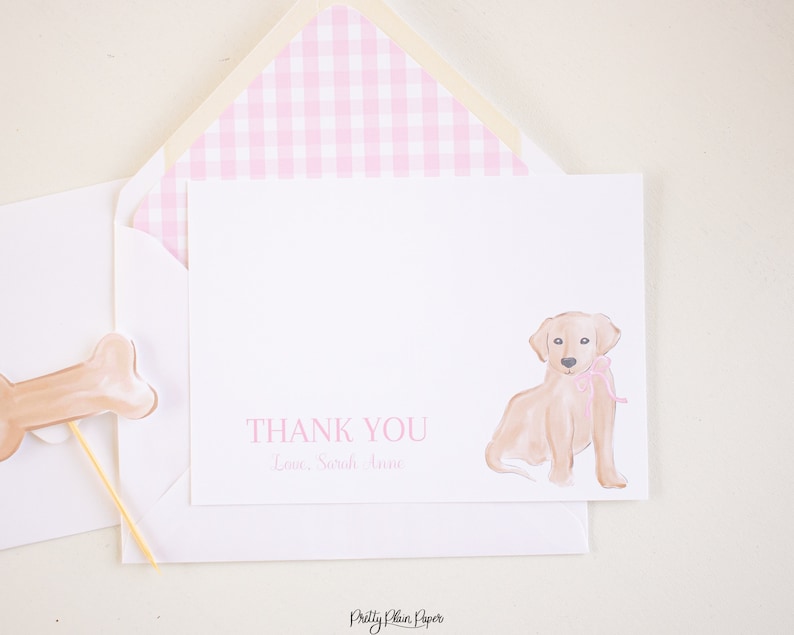 K&ouml;nnte beinhalten: Eine wei&szlig;e Dankeskarte mit einem rosa karierten Umschlag. Die Karte zeigt eine Aquarell-Illustration eines Golden Retriever-Welpen mit einer rosa Schleife. Der Text "THANK YOU" und "Love, Sarah Anne" ist in rosa auf der Karte gedruckt.