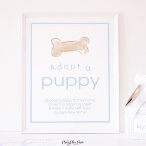 May include: A white framed sign with a blue border and the text "Adopt a puppy". The sign features a cartoon bone and instructions to choose a puppy, fill out an adoption sheet, and make a collar with the puppy's new name.
