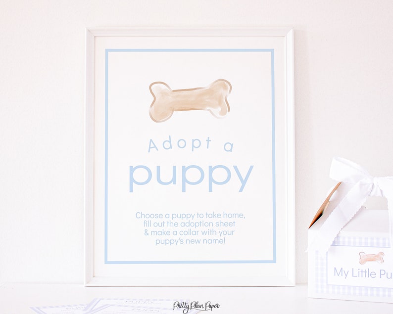 May include: A white framed sign with a blue border and the text "Adopt a puppy". The sign features a cartoon bone and instructions to choose a puppy, fill out an adoption sheet, and make a collar with the puppy's new name.