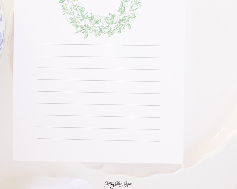 May include: A white sheet of paper with a green floral wreath at the top and lined with horizontal lines. The text "Pretty Plain Paper" is at the bottom of the page.