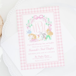 May include: A pink and white gingham patterned invitation with a floral and animal illustration. The invitation reads "Hannah's First Chapter" and includes event details. The invitation is on a white envelope and plate.