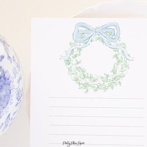 May include: A white card with a green and white wreath with a light blue bow on top. The card has lined paper for writing and the text "Pretty Plain Paper" at the bottom.