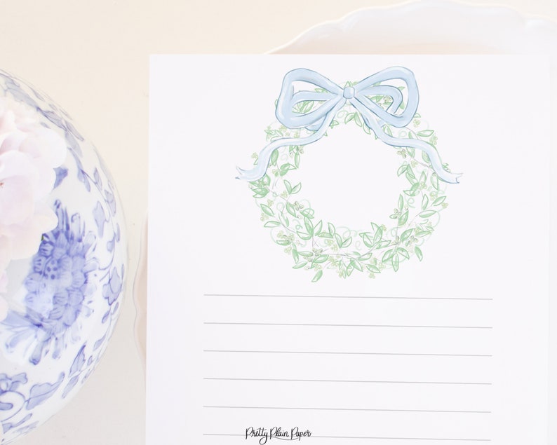 May include: A white card with a green and white wreath with a light blue bow on top. The card has lined paper for writing and the text "Pretty Plain Paper" at the bottom.