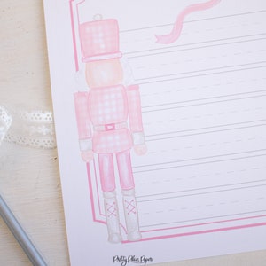 May include: A pink and white gingham nutcracker with a pink ribbon and a white background. The nutcracker is standing on a white surface. The text "Pretty Plain Paper" is at the bottom of the image.