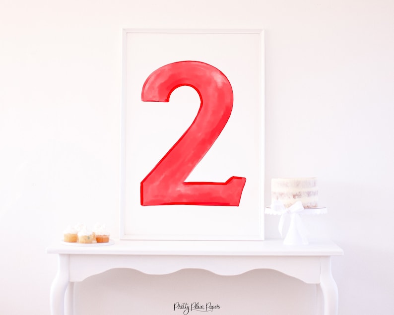 May include: A framed watercolor painting of the number two in red. The number is large and fills the frame. The frame is white and has a simple design.