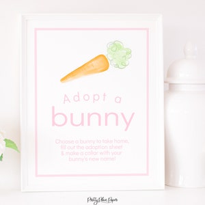 May include: A white sign with pink text that says "Adopt a bunny". There is a watercolour illustration of a carrot with green leaves on the sign. The text below the title says "Choose a bunny to take home, fill out the adoption sheet & make a collar with your bunny's new name!"