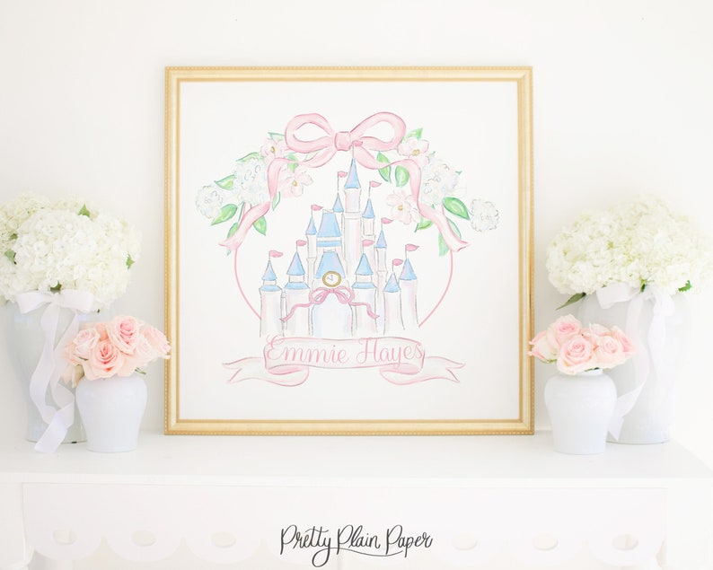 Puede incluir: Una pintura de acuarela de un castillo rosa y azul con un lazo rosa y flores blancas. El castillo tiene una torre del reloj y banderas. La pintura est&aacute; enmarcada en oro y tiene el nombre "Emmie Hayes" escrito en una cinta rosa.