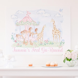 May include: A watercolour print depicting a carousel with horses, giraffes, and rabbits in a whimsical scene. The artwork uses soft pastel colours and includes the text "Junnie's First Go-Round" in pink.