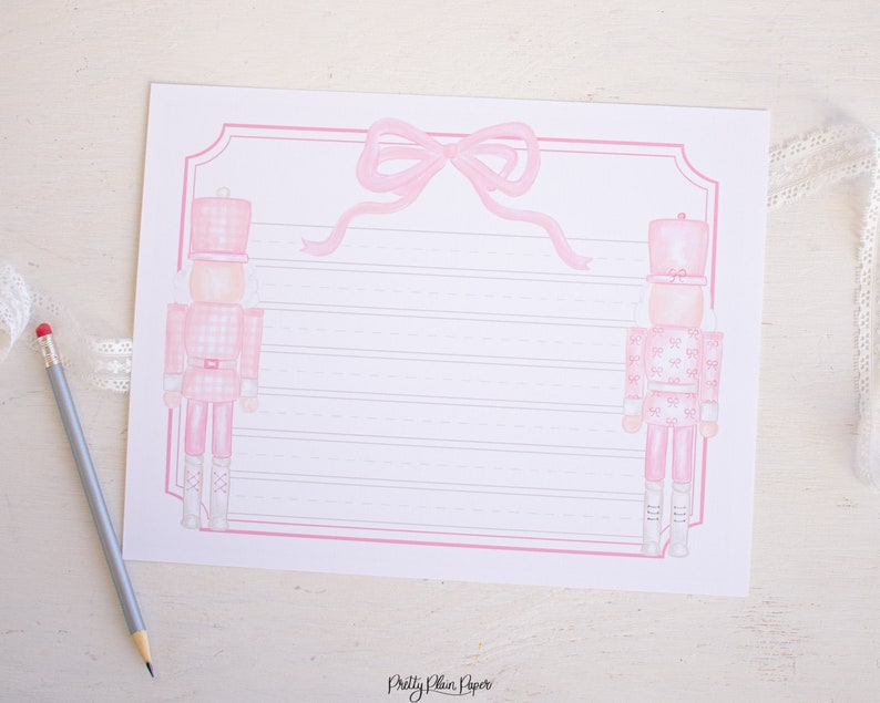 May include: Pink and white printable stationery featuring two pink nutcracker soldiers with a pink bow at the top. The paper has pink lines for writing.