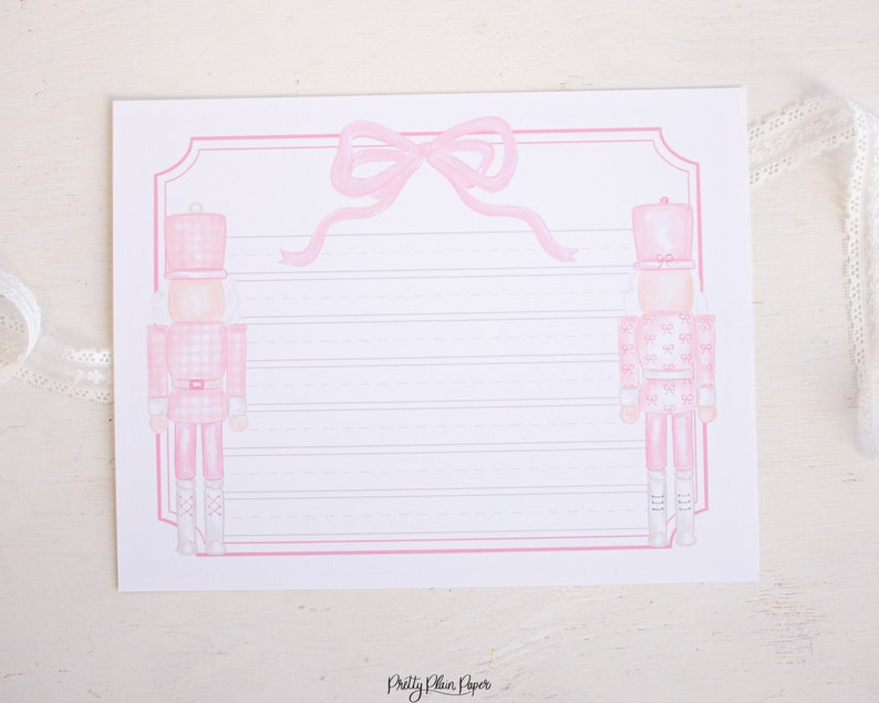 May include: Pink and white printable stationery featuring two pink nutcracker soldiers with a pink bow at the top. The paper has lined writing space.