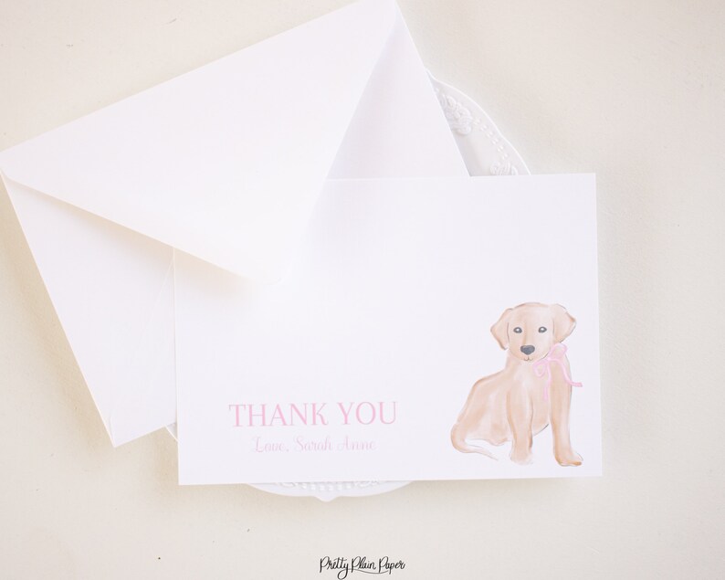 K&ouml;nnte beinhalten: Eine wei&szlig;e Dankeskarte mit einer Aquarell-Illustration eines Golden-Retriever-Welpen, der eine rosa Schleife tr&auml;gt. Der Text "THANK YOU" und "Love, Sarah Jane" ist in rosa gedruckt.