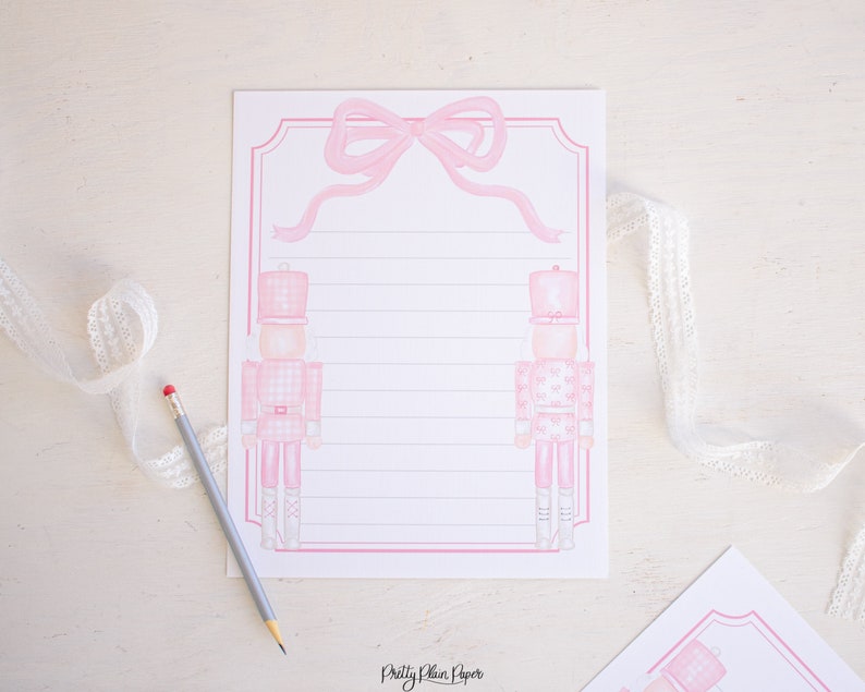 K&ouml;nnte beinhalten: Rosa und wei&szlig;er druckbarer Briefpapier mit zwei rosa Nussknacker-Soldaten mit einer rosa Schleife oben. Das Papier hat rosa Linien zum Schreiben.